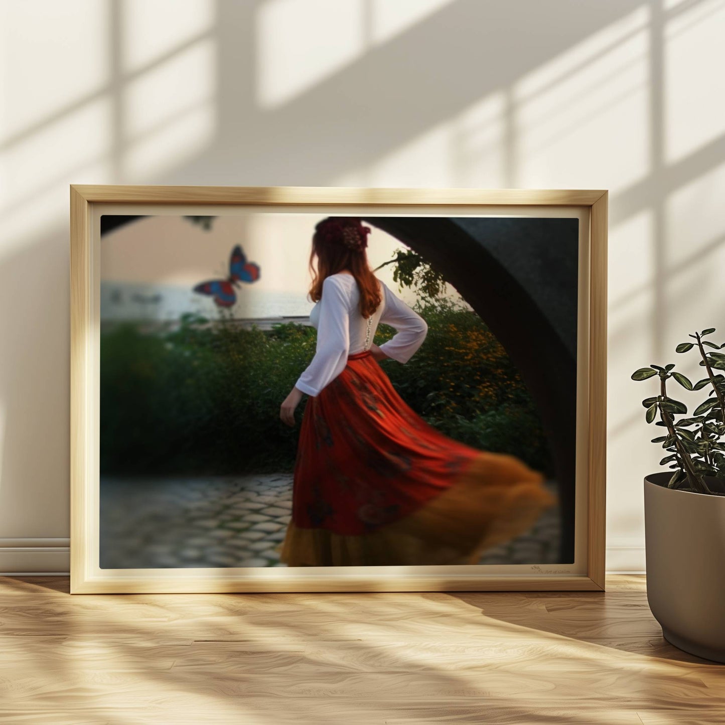 Eine Frau in folkloristischer Kleidung tanzt auf Kopfsteinpflaster durch einen Steinbogen, im Hintergrund ein großer Schmetterling am Meer.. Rahmen natur 40x30