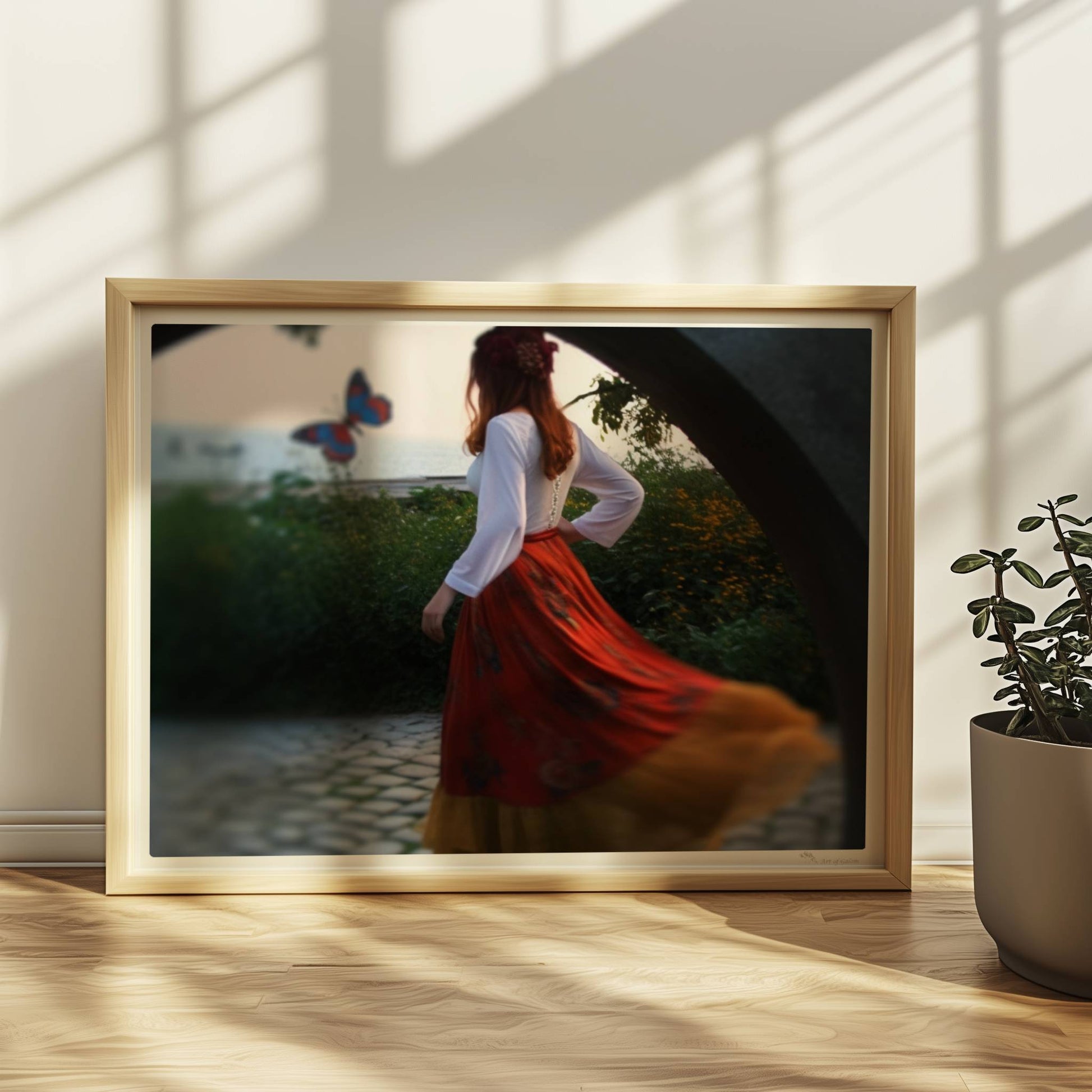 Eine Frau in folkloristischer Kleidung tanzt auf Kopfsteinpflaster durch einen Steinbogen, im Hintergrund ein großer Schmetterling am Meer.. Rahmen natur 40x30