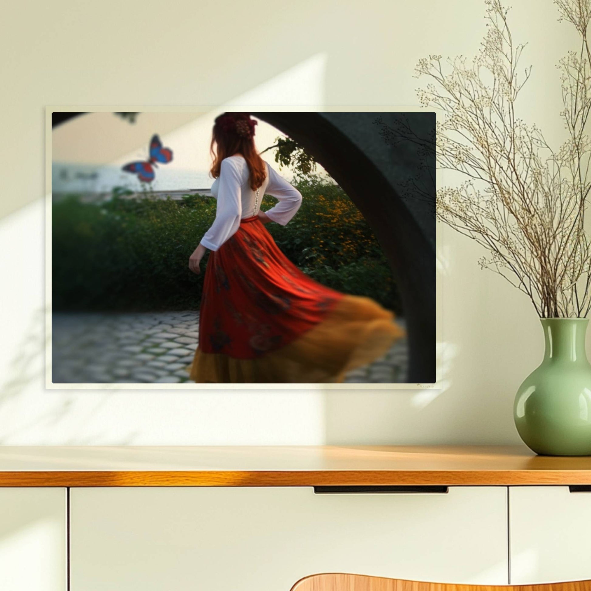 Eine Frau in folkloristischer Kleidung tanzt auf Kopfsteinpflaster durch einen Steinbogen, im Hintergrund ein großer Schmetterling am Meer.. Ohne Rahmen 70x50