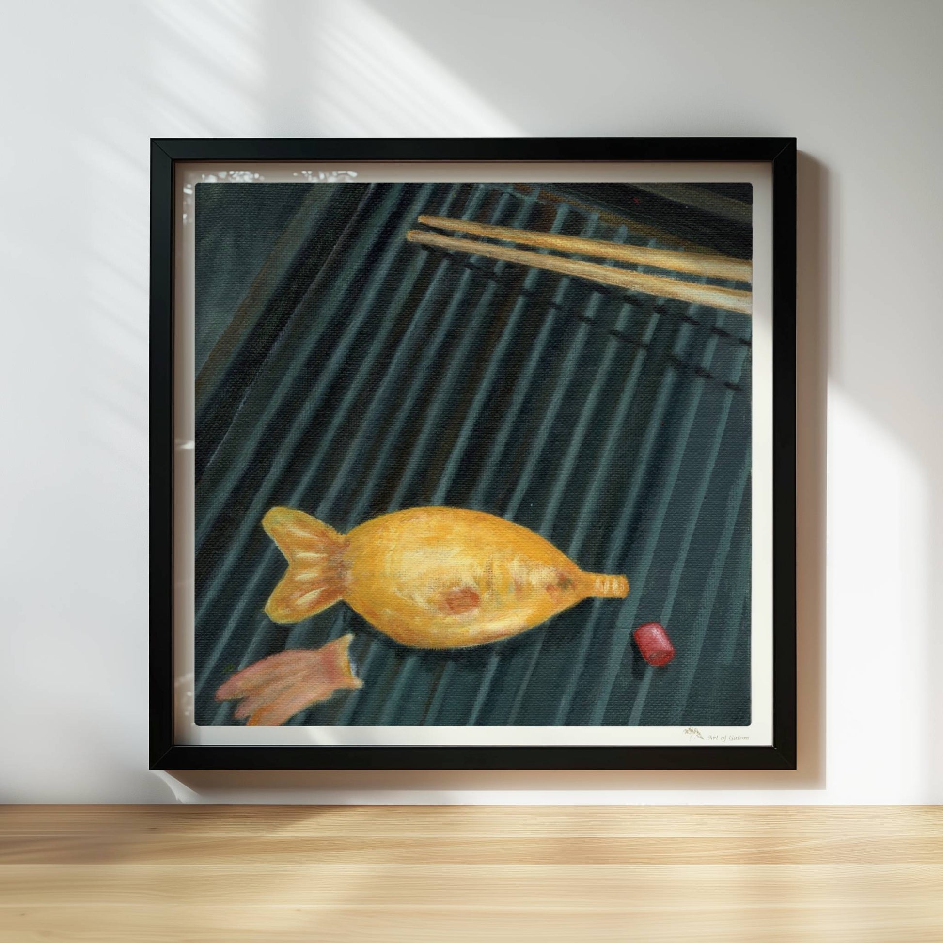 Goldener Fisch auf Sushi-Matte mit Stäbchen, surreal inszeniert.. Rahmen schwarz 30x30