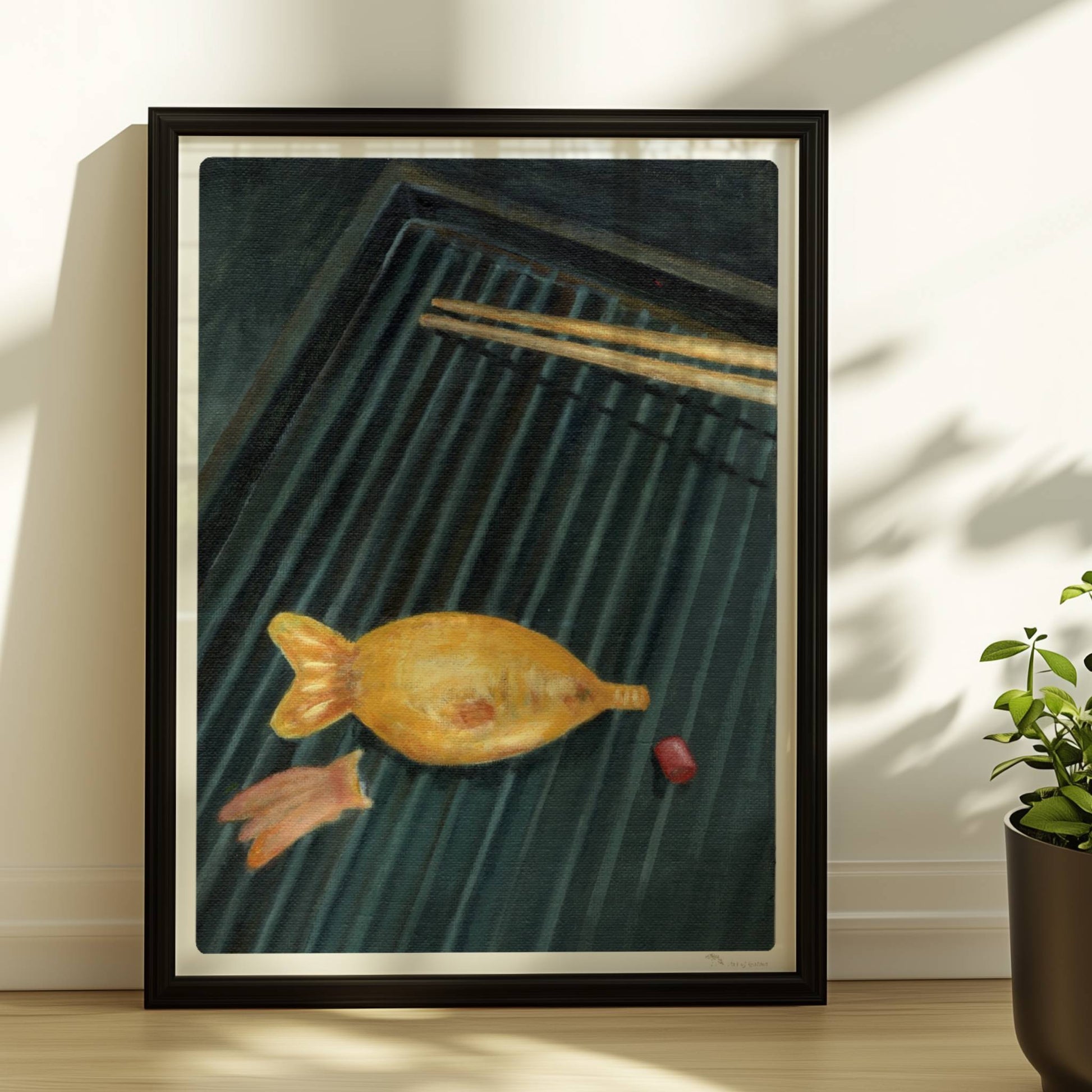 Goldener Fisch auf Sushi-Matte mit Stäbchen, surreal inszeniert.. Rahmen schwarz 30x40