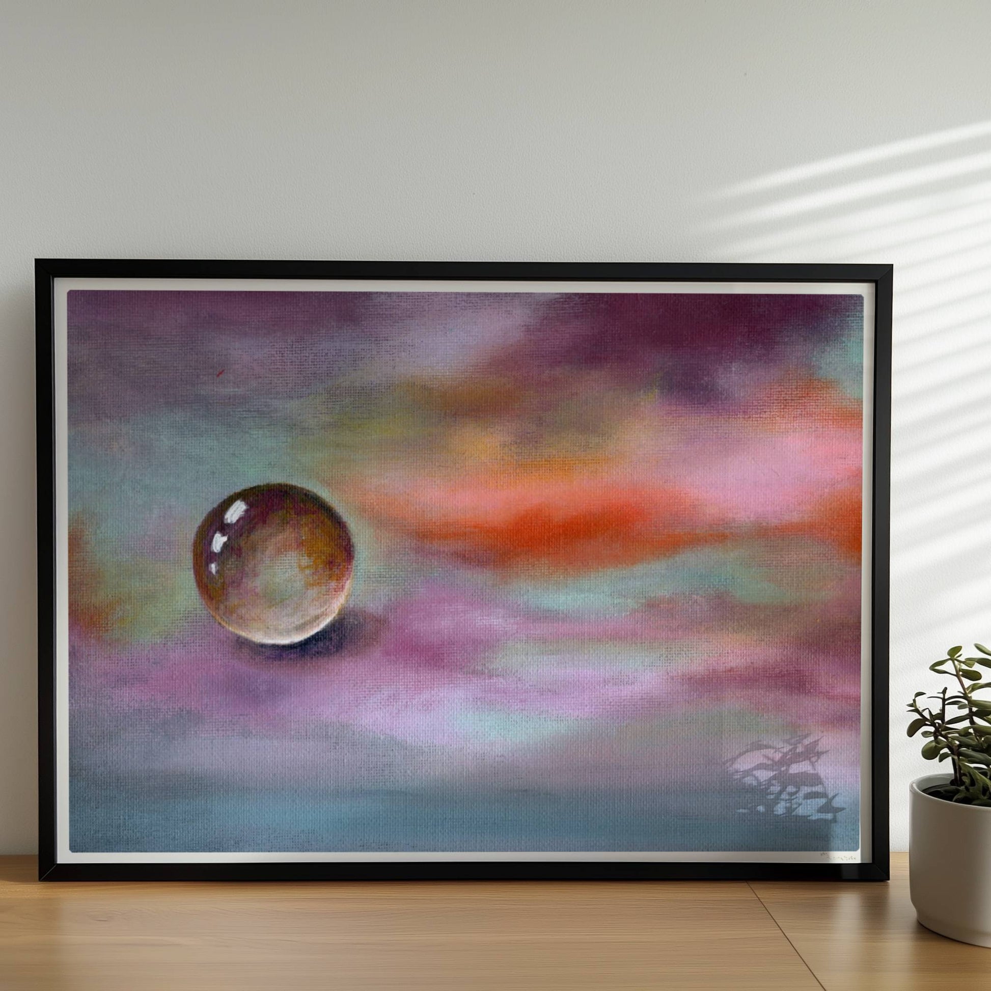 Schwebende Glaskugel vor farbenfrohem Himmel in Lila und Orange.. Rahmen schwarz 70x50
