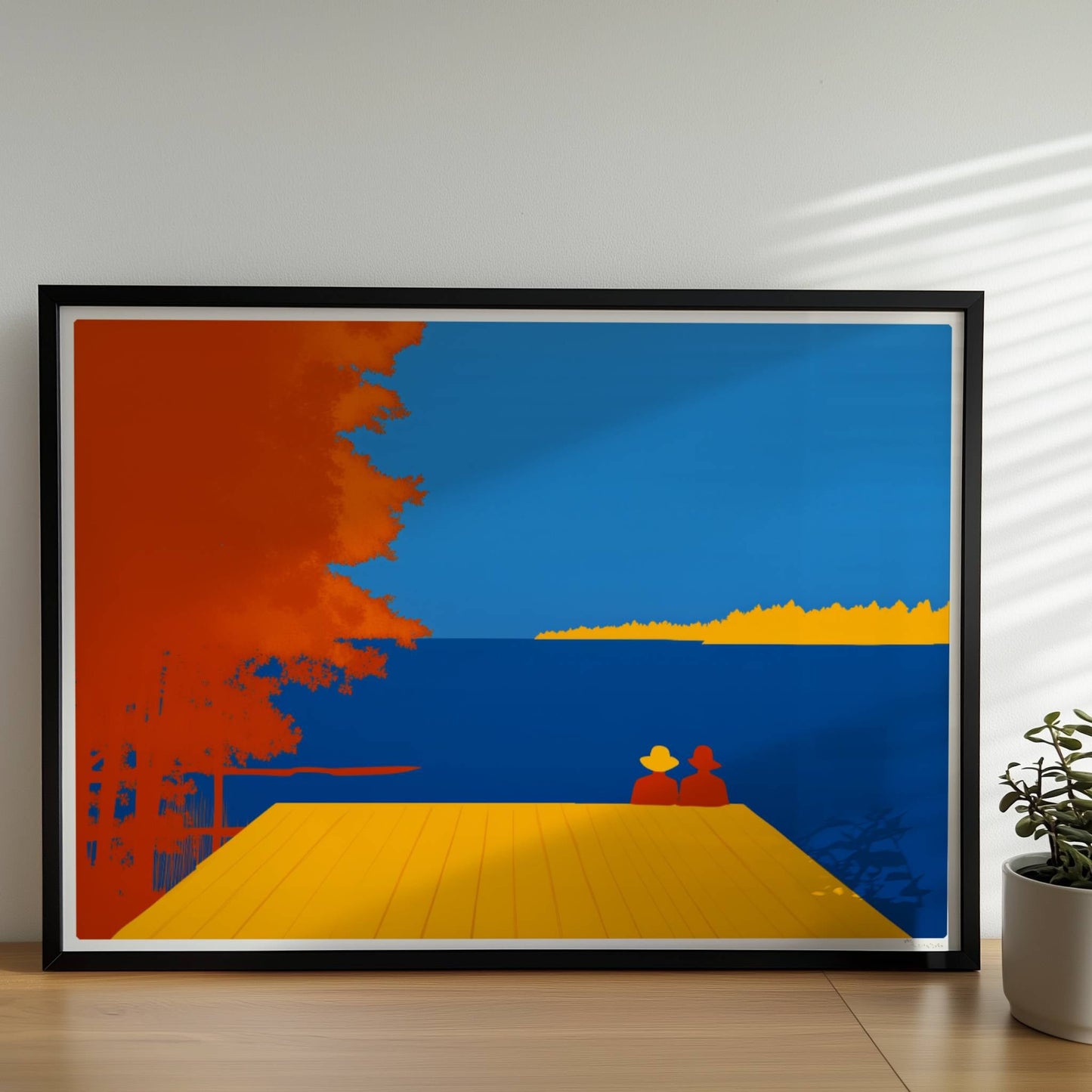 Zwei Personen auf einem Steg mit Blick auf einen leuchtend blauen See, flankiert von herbstlichen orangefarbenen Bäumen.. Rahmen schwarz 70x50